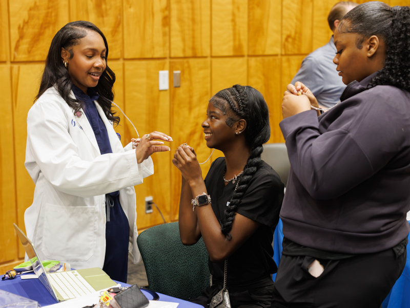 Carrington Williams, a student in the School of Graduate Studies in the Health Sciences, performs a hearing care test on Hattiesburg High School juniors Nyla Flowers and Alexis Maye during Discovery Day.