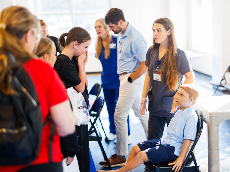 Jennifer Harrison, health professionals educator in the Department of Advanced Biomedical Education, explains the various functions of the HAL pediatric patient simulator with students in the Academy of Health Sciences at Pelahatchie High School during Discovery Day.