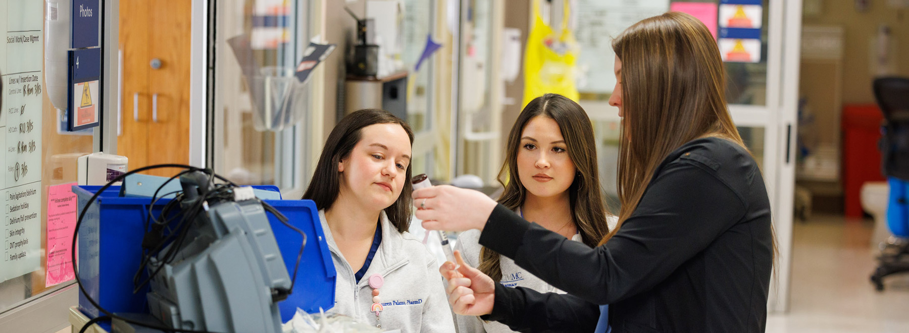 At the nurses' station, a resident fills a syringe while two other residents look on.