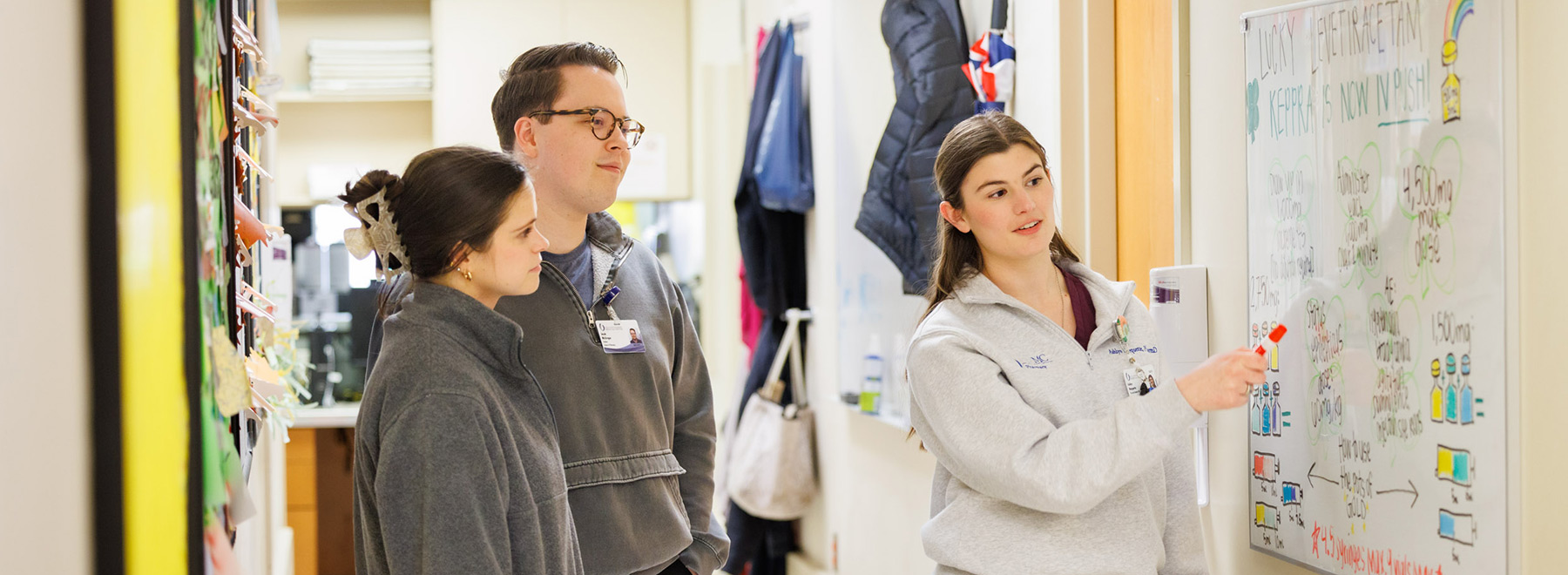 A pharmacy resident points out information on a whiteboard while two other residents look on.