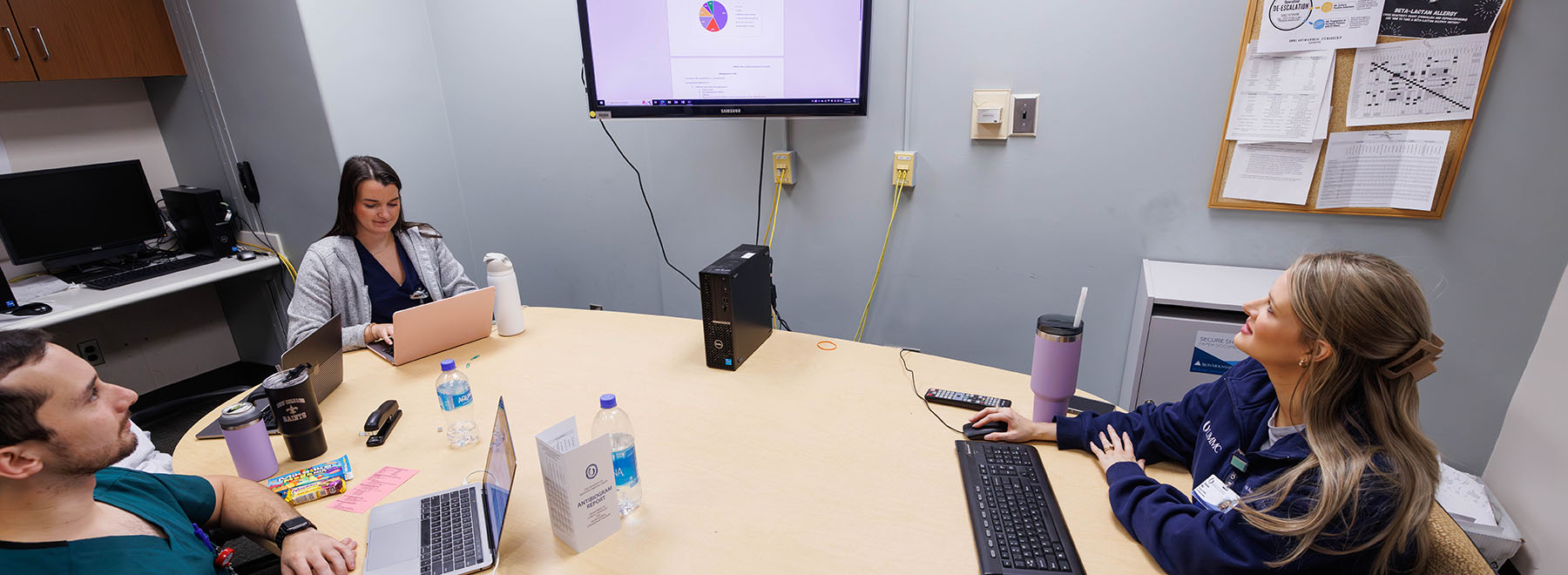 Three UMMC-based pharmacy residents sit around table while reviewing a presentation on a monitor.