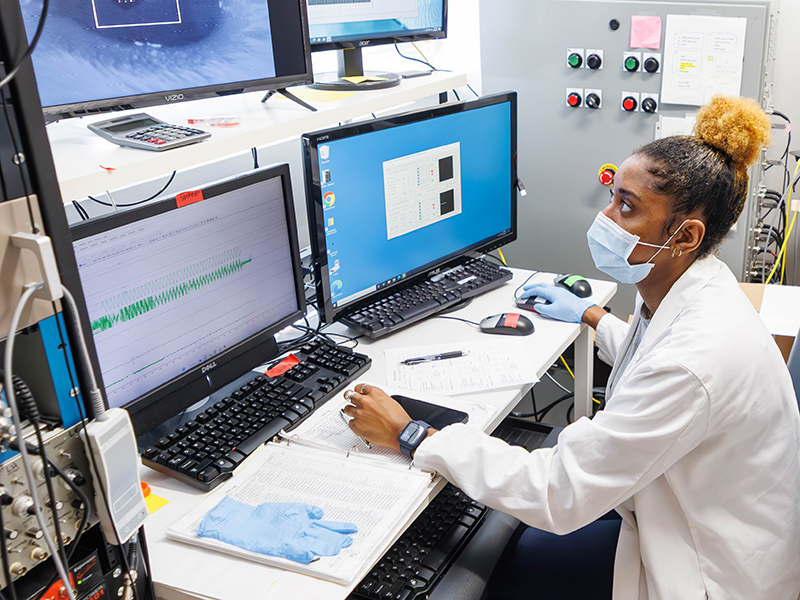 Research associate Dr. Raven Riley in the lab viewing results on four computer monitors.