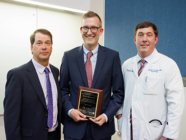 Pictured from left to right: Dr. David Stec, Dr. Barry A. Borlaug holding a plaque in his honor, and Dr. Michael Hall.