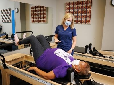 A physical therapist in blue scrubs works with a patient who is lying on her back as she uses exercise equipment.