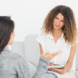 Two women sitting together, facing each other with one listening as the other speaks.