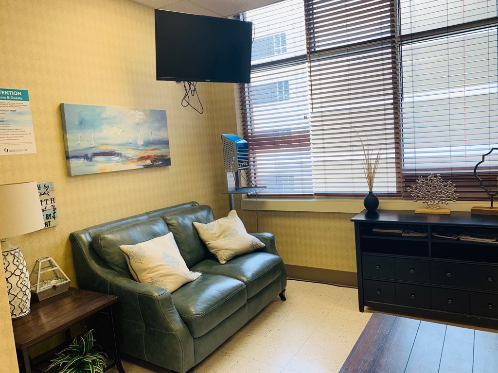 A couch underneath a large screen TV, with a credenza beneath a window.