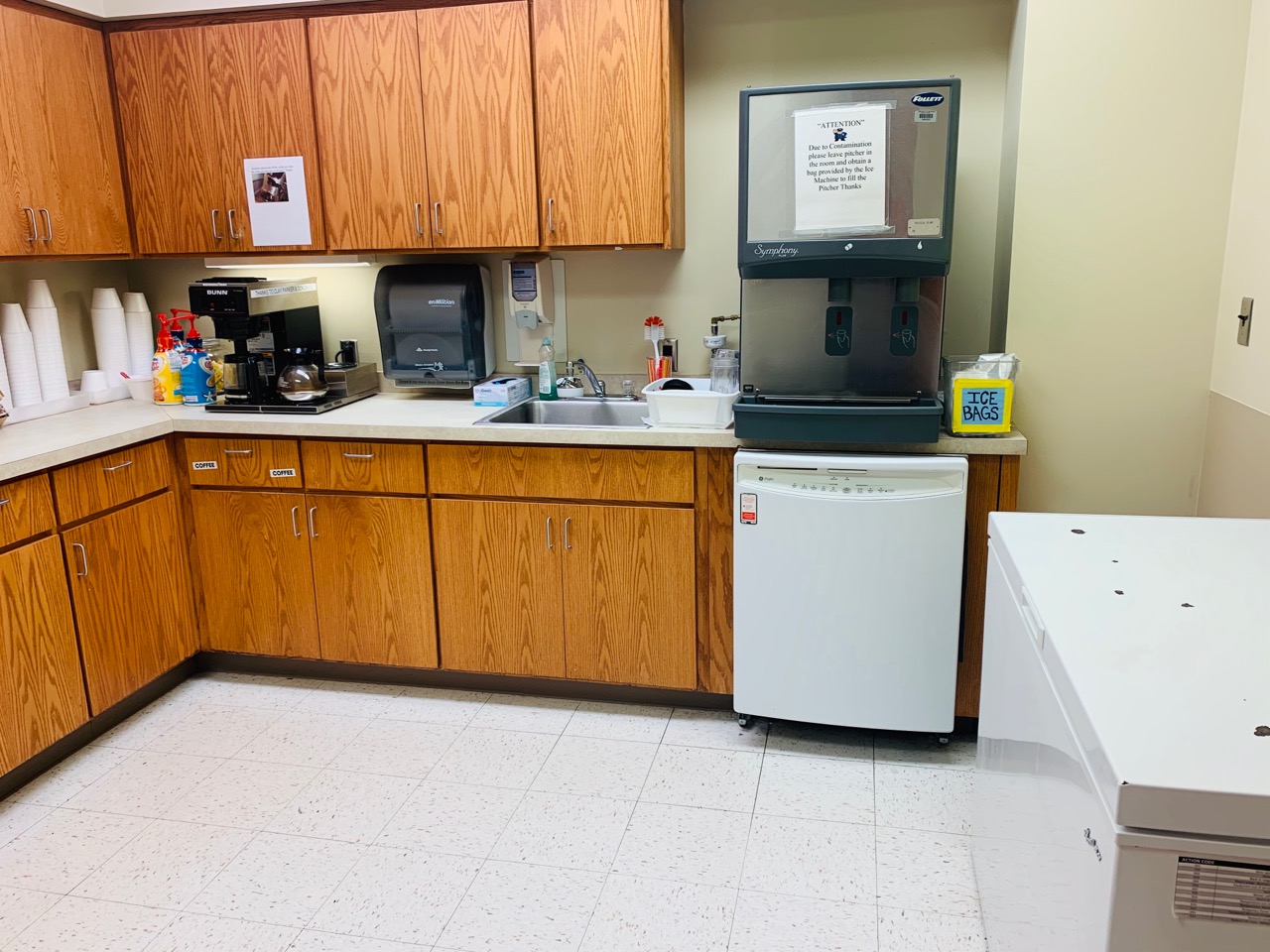 Kitchen with a coffee pot, sink, several cabinets and a large ice maker.