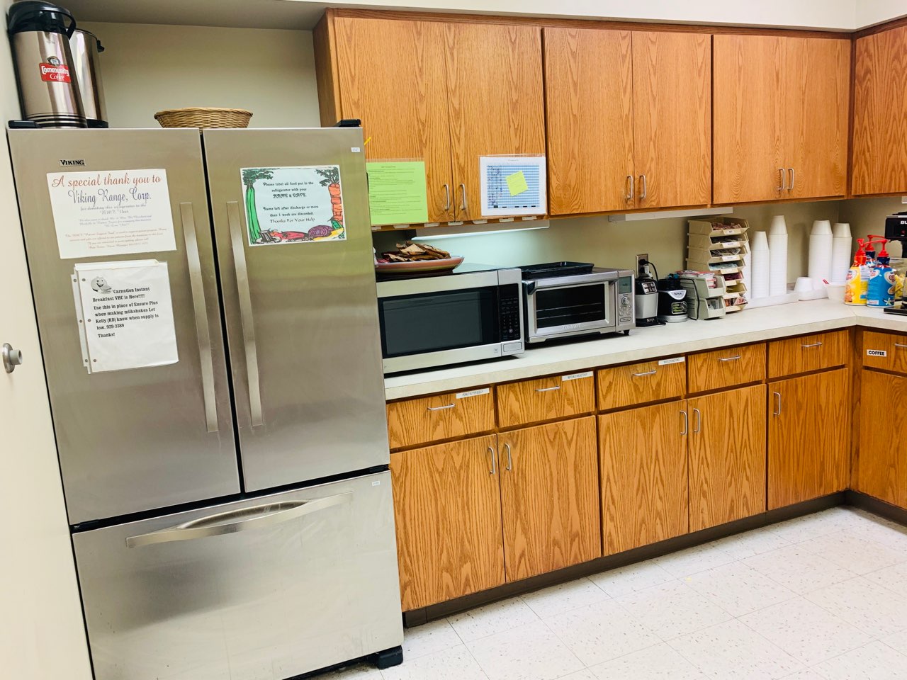 A large stainless steel refrigerator stands next to many cabinets on which are a microwave oven and toaster.