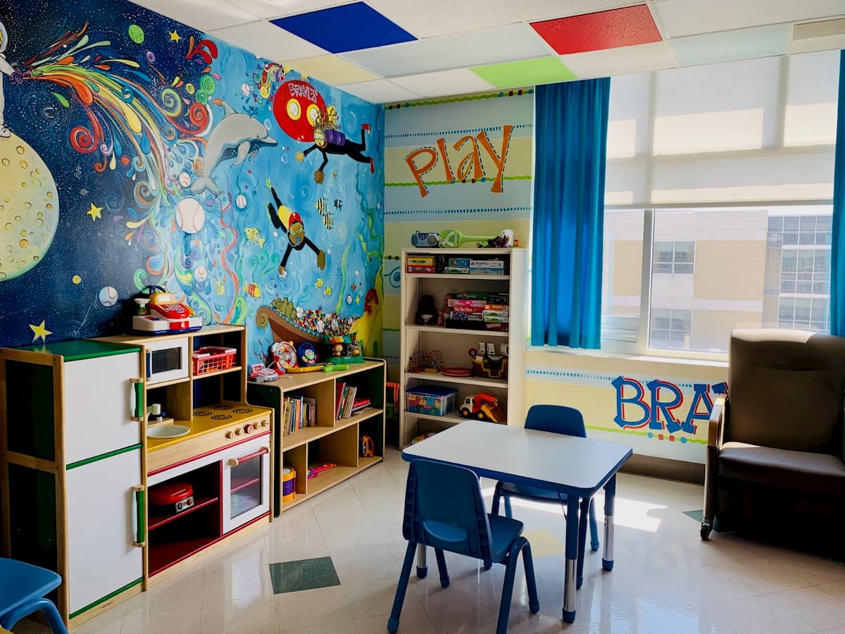 A colorful playroom is filled with kid-sized furniture, toys and a make-believe kitchen.