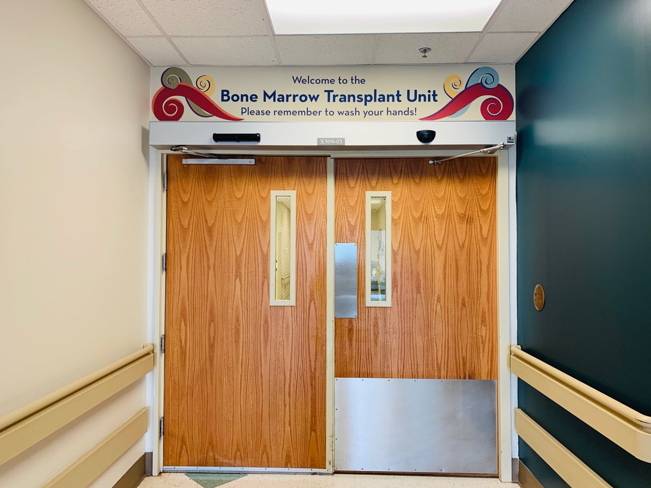 Double doors leading to the Bone Marrow Transplant Unit with a sign above that says Welcome to the Bone Marrow Transplant Unit. Please remember to wash your hands.