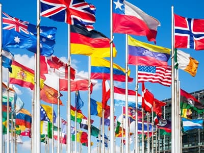 A large group of flags from many different countries wave in front of a bright blue sky.