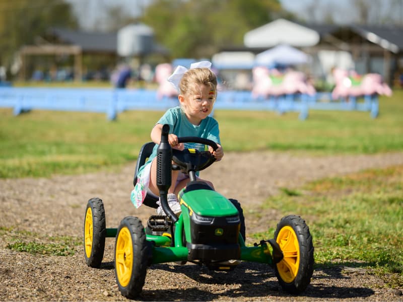 A girl wearing a white bow rides a toy at Family Fun Day 2026.