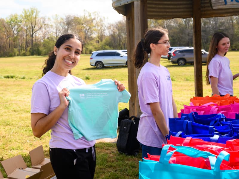 A volunteer working at registration shows participant t-shirts for Family Fun Day 2026.