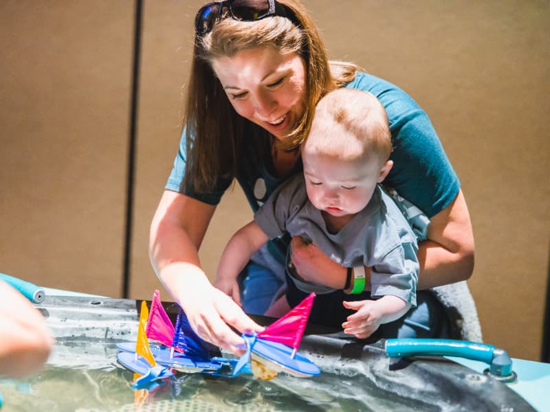 A mom helps her toddler play with a sailboat during Family Fun Day