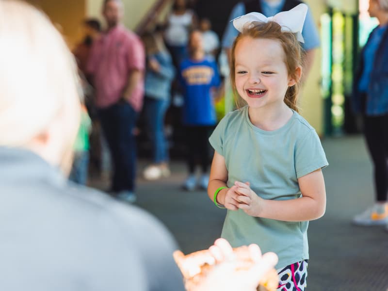 A girl with a white bow in her hair looks at a snake during Family Fun Day