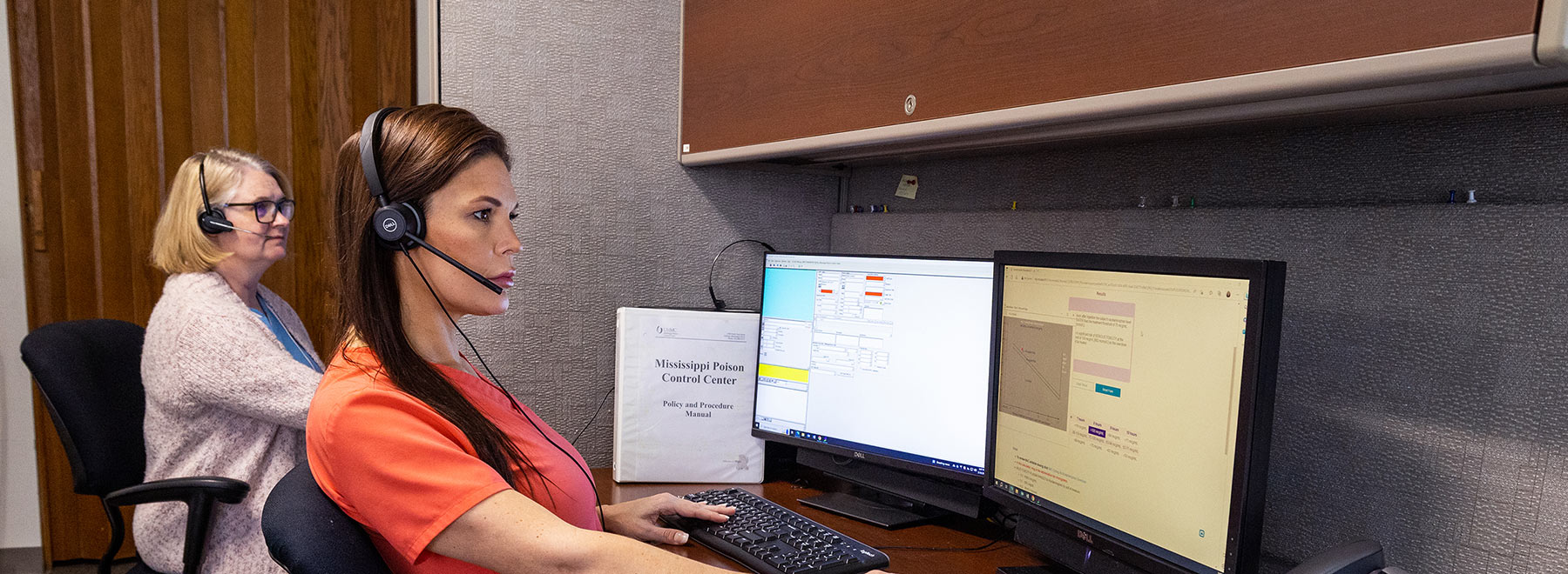 Two Mississippi Poison Control Center employees at their workstations taking calls.