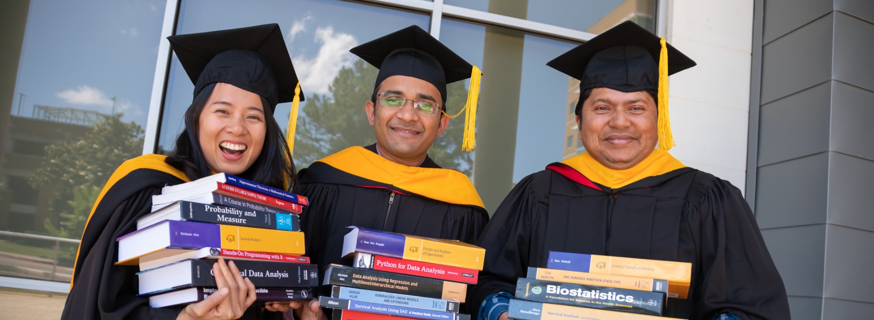 Three students in graduation robes smiling.