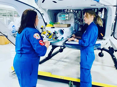 Two Neonatal Transport team members conversing in front of a helicopter.