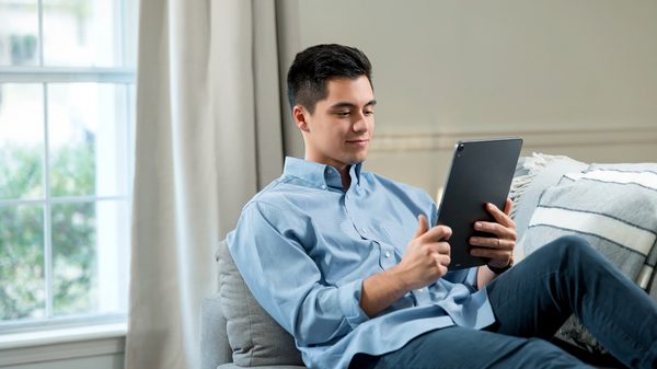 Person sitting on couch reads tablet computer.