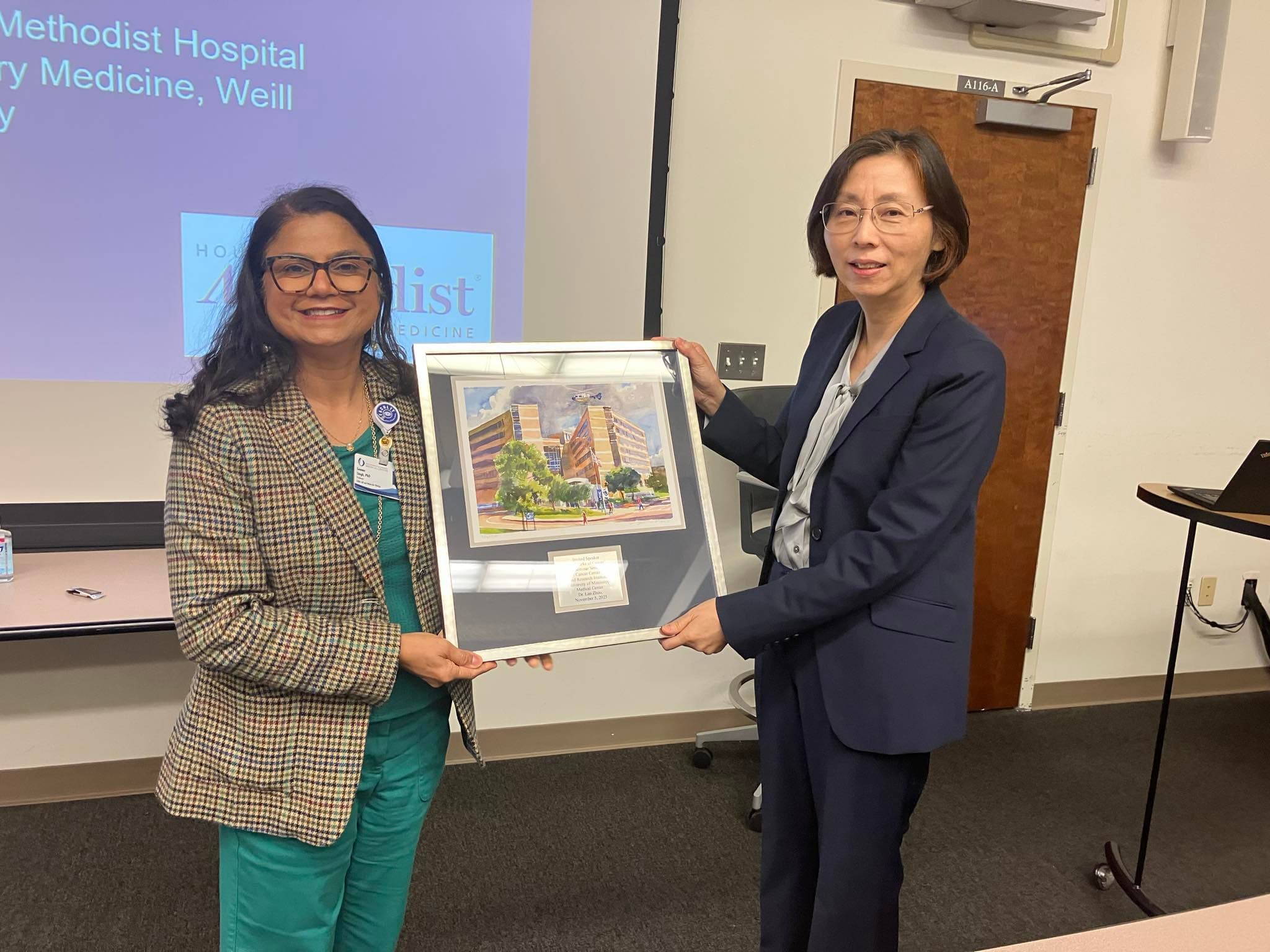 Dr. Seema Singh, left, professor of cell and molecular biology and associate director of education and training at CCRI, presents Dr. Lan Zhou with a framed watercolor of UMMC.