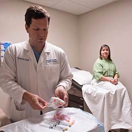 Doctor prepares syringes and vials as patient sitting on exam table looks on.