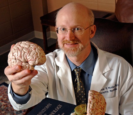 Dr. Thomas Mosley holding up plastic model of brain.
