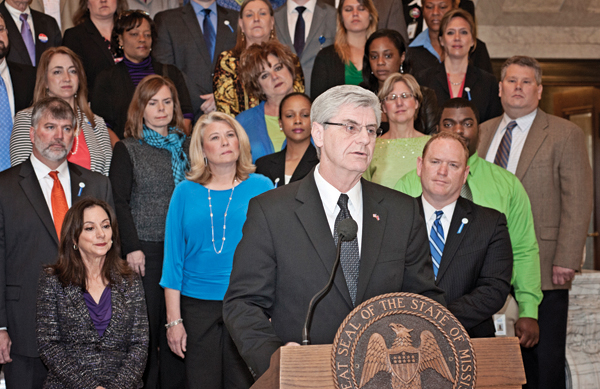 Gov. Phil Bryant addresses a crowd at an announcement of the Children's Collaborative, a partnership between UMMC and Mississippi Children's Home Services. Joining him are Dr. Susan Buttross, front row left, Dr. John Damon, front row right, CEO of MCHS, and employees of MCHS and Medicaid.