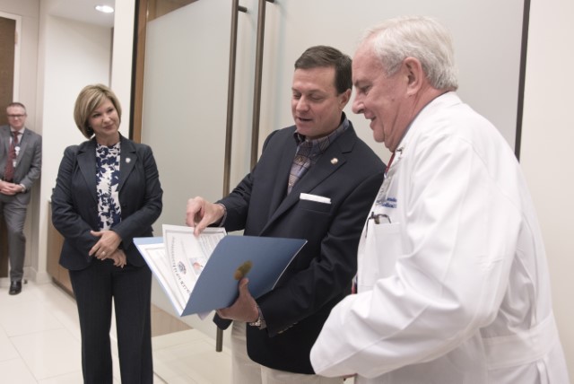 Mississippi State Sen. Walter Michel, center, presents the House and Senate resolution to Dr. Michael Henderson while Dr. LouAnn Woodward, vice chancellor for health affairs, looks on.