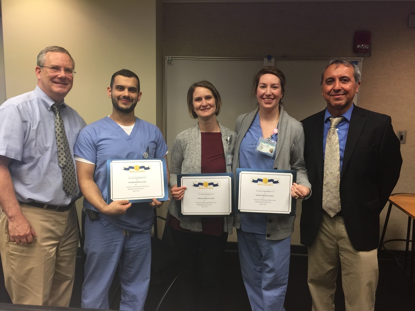 Dr. Robert Brodell, left, professor of dermatology and interim chair of pathology, and Dr. Christian Gomez, right, associate professor of pathology and interim director of research, congratulate pathology residents who received awards during the Research Day event, from left, Dr. Anas Bernieh, Dr. Kristen Adams and Dr. Katie Tumminello.