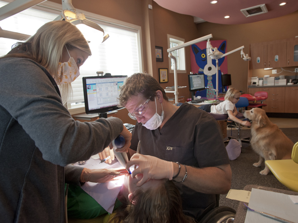 Dental assistant Nikki Latham assists as Perkins seals the teeth of patient Karra Mae Johnson of Cedar Bluff. Behind them, patient Mallorie Stevens gets some petting time with Sophie.