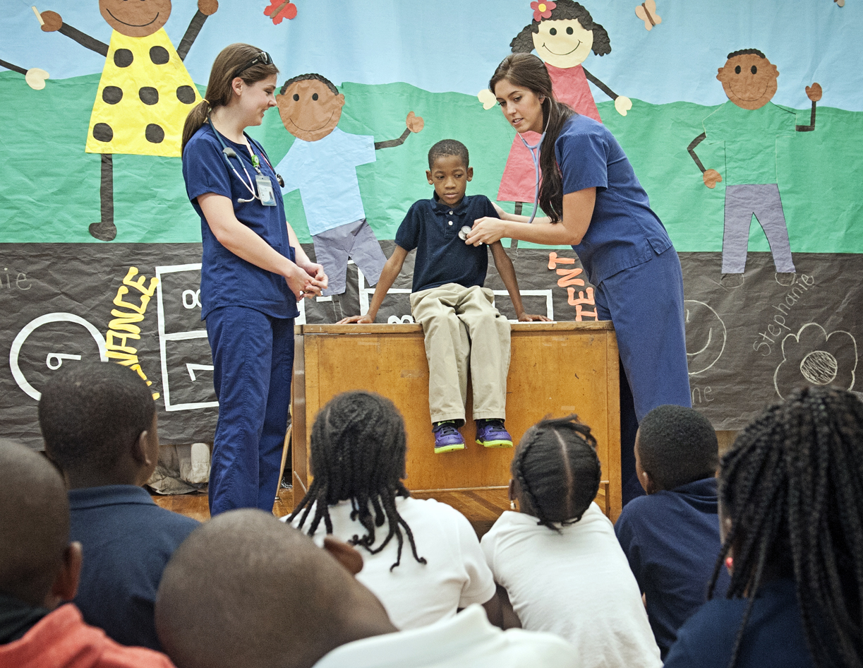Senior nursing students Kelly Wilson, left, and Julia Lake Landrum, right, demonstrate how to check third-grader Adyn Bolds' vital signs for his classmates at Brown Elementary School.