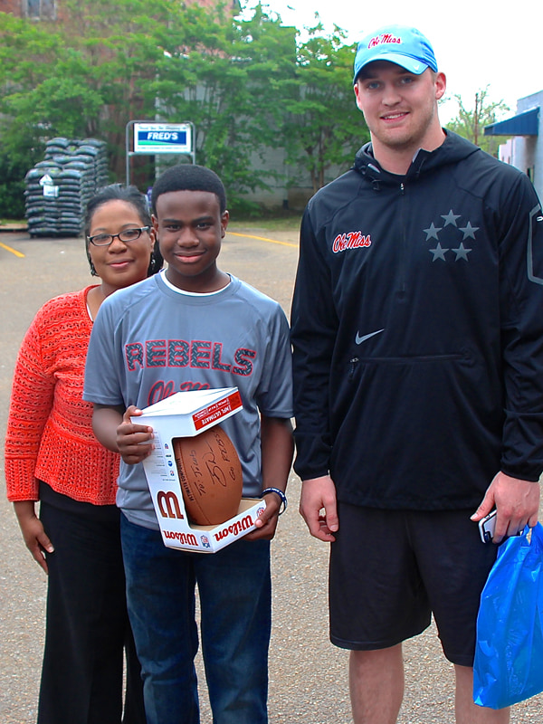 Jacob Partlow of Jackson holds on to his new autographed football from former Ole Miss quarterback Bo Wallace. With help from Jacob's mom, Olevia Williams, left, Wallace surprised Jacob with the football Friday afternoon.