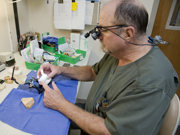 Working with fellow maxillofacial prosthetics specialist Gary Swedenburg, Bill Graham (pictured) checks the color and contour of a bridge that is part of a permanent prosthesis for a patient who underwent Jaw in a Day surgery.