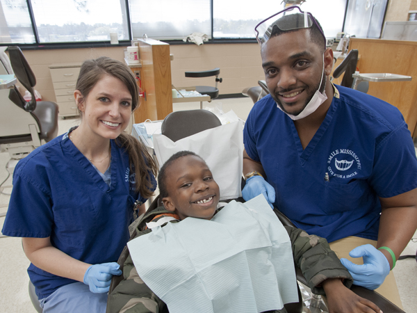 Second-year dental student Brittany Varney, left, and third-year dental student Christopher Cathey, right, put a grin on Galloway Elementary student Antwuan Williams' face .
