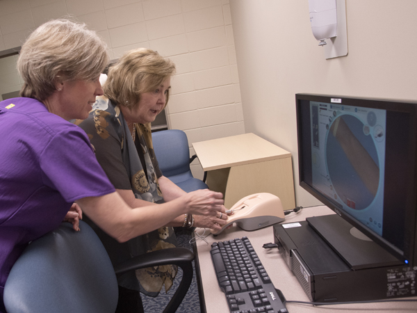 Robyn MacSorley, assistant professor in the School of Nursing, assists Vandergriff as she tries out the Virtual I.V. used to train students in the SON.