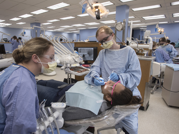 Dental hygiene students Holly Loft, left, and Meredith Loper, right, clean patient Melissa Smith's teeth.