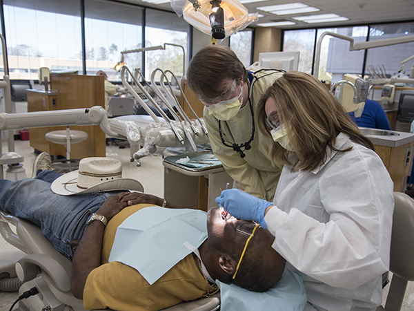 Deming-Jefcoat checks over the dental cleaning of D3 Jay Ballard on patient Hubert Miller of Bryam.