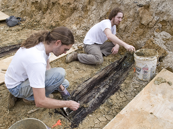 In this photo from 2013, Mississippi State University archaeologists Derek Anderson and Forrest Follett remove soil from the lid of one of more than 35 graves.