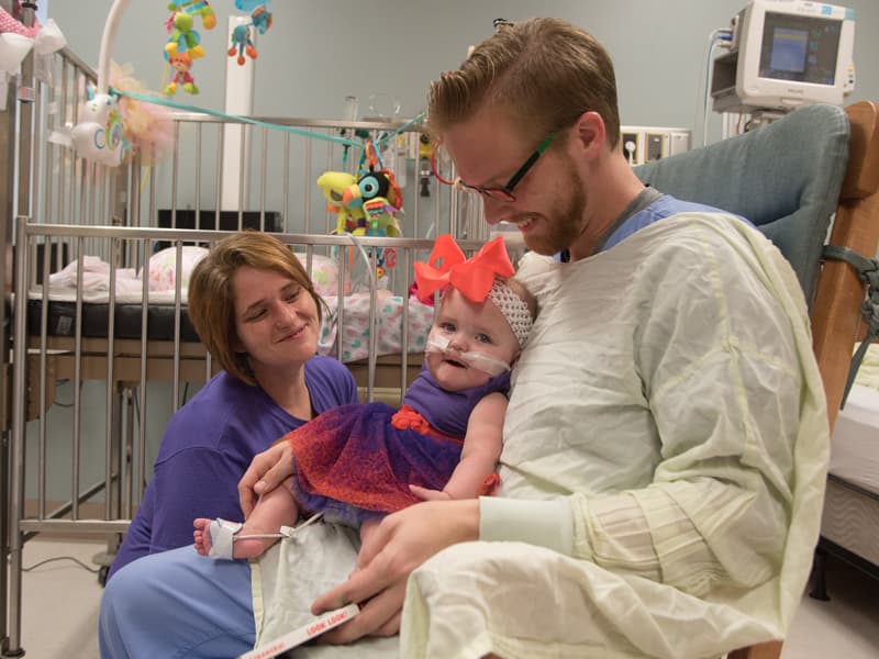 While Sonny Gunn, a second-year occupational therapy student, rocks Deavannah Bass, the infant's mother, Deanna, coaxes a smile from her toddler during the child's last day in the Neonatal Intensive Care Unit in the Winfred L. Wiser Hospital for Women and Infants.