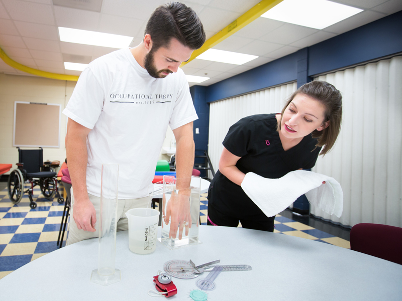 Third year OT students Ferris McGuire, left as simulated patient, and Amy Claire Cox, demonstrate assessing edema through the use of volumetrics.