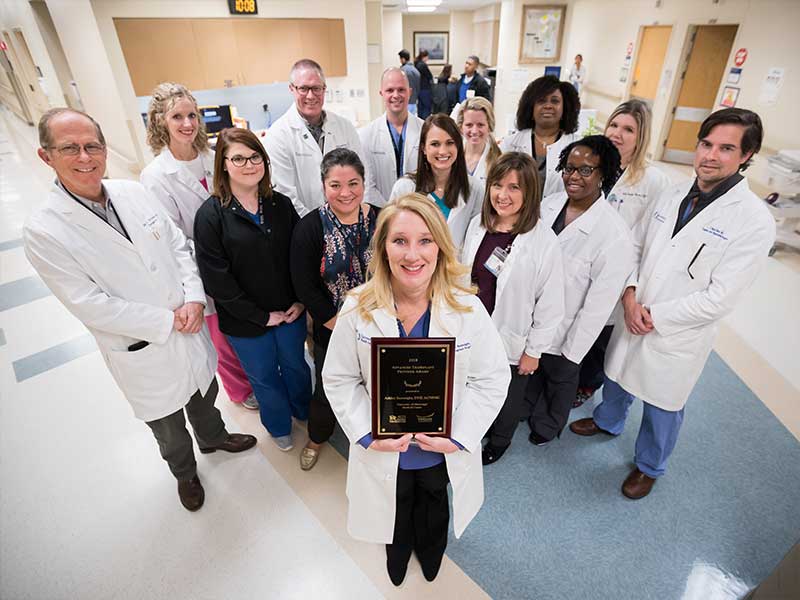 Ashley Seawright proudly displays her Advanced Transplant Provider Award in front of some of her team members, back row from left, Dr. James Wynn, Toy Wolfe, Dr. Christopher Anderson, Steve Harvey, Hart Berry, Lanecko Bailey, Julie George, and Dr. Mark Earl, and front row from left, Amanda Roberts, Dr. Felicitas Koller, Jodie Kilby, Terri Traylor, Sherie Brock.