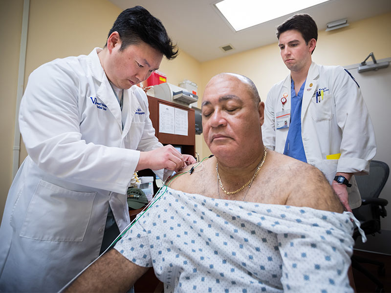 Dr. Hyung Kim, left, assistant professor of neurosurgery, attaches electrical leads to acupuncture needles in patient John Keys' shoulders while Seth Knight, right, a third-year medical student, looks on during a treatment at the G. V. "Sonny" Montgomery VA Medical Center.