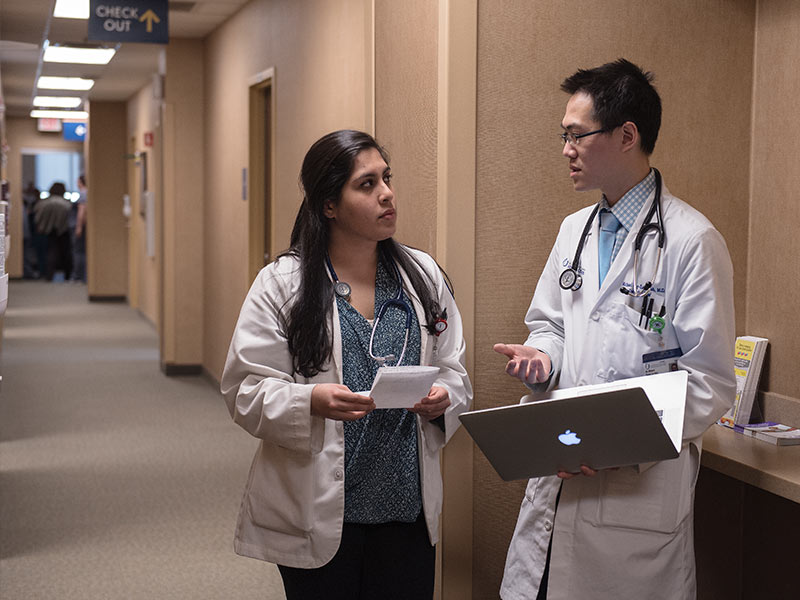Dr. Michael Yeung-Lai-Wah consults a patient's electronic health record on his laptop as he discusses treatment with Pooja Chawla, a third-year medical student in her family medicine rotation.
