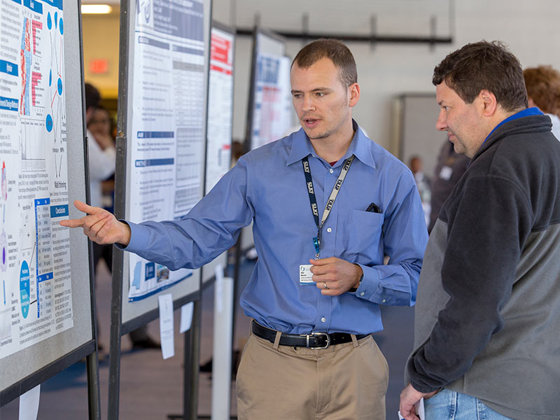 Dr. Alan Mouton, postdoctoral research fellow, discusses his work with Dr. Damian Romero, associate professor of biochemistry, at Department of Medicine Research Day. Mouton won first place for his poster presentation.