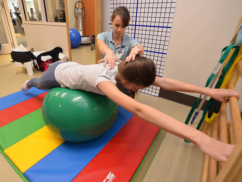 Methodist Rehabilitation Center physical therapist Elizabeth Rich helps Wilbourn elongate her spine while deep breathing over an exercise ball during one of her Schroth Therapy sessions at Methodist Outpatient Therapy in Ridgeland.