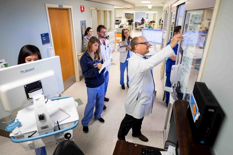 Dr. Jay Shake, right, professor of cardiothoracic surgery and medical director of the Wallace Conerly Critical Care Hospital, writes patient details on a board outside a CCU patient room during rounds.