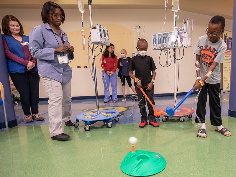 Batson Children's Hospital patients Keydarius Taylor, right, and Lee Barner take turns putting in the hospital lobby as child life assistant Michelle Chambers looks on.