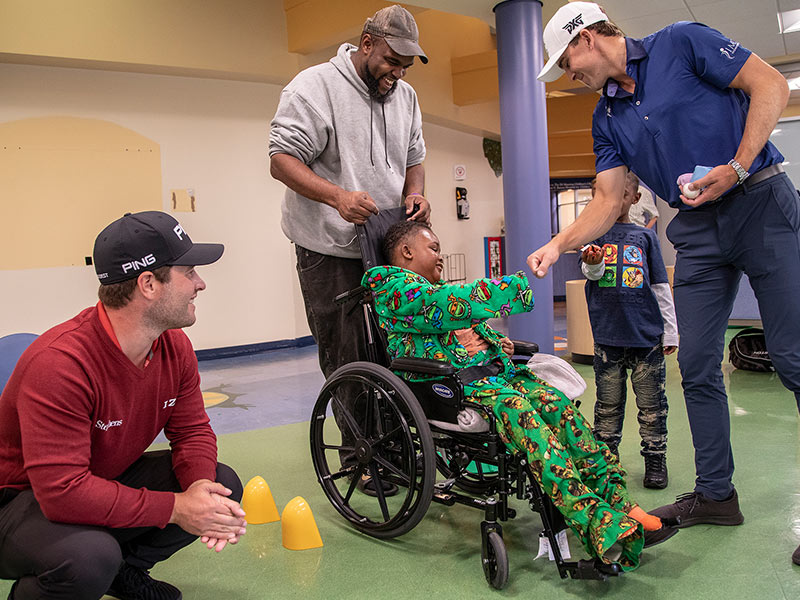 Zayveon Bounds gives professional golfer Scott Langley a fist bump as fellow Sanderson Farms Championship competitor David Lingmirth looks on.