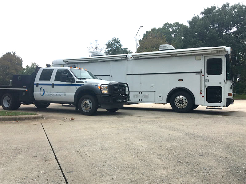 A Mississippi Center for Emergency Services truck and UMMC ambulance bus await deployment in a Florida parking lot during Hurricane Michael relief efforts.