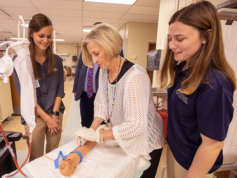 Becky Tustain practices starting an IV in the simulation lab with nursing students Kathryn Dooley, left, and Katie French, right.